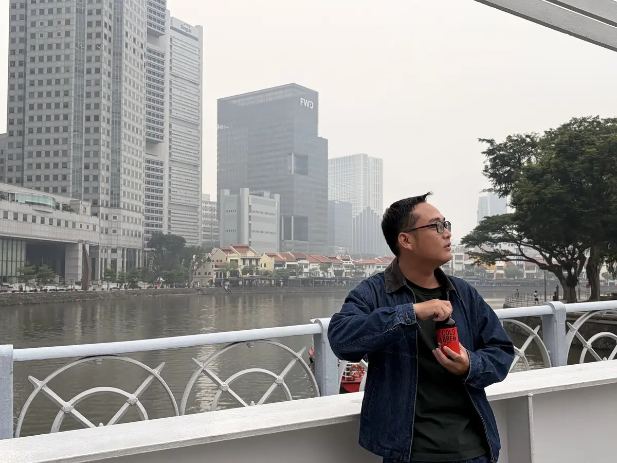 Harry standing by the Singapore River with the city skyline behind him.